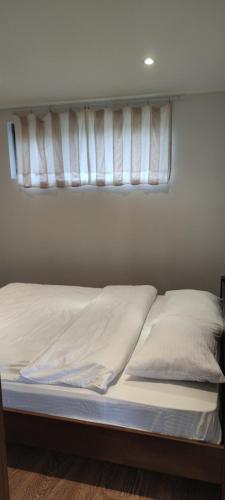 a bed with white sheets and pillows under a window at West Wood ApartHotel in Knyagynya