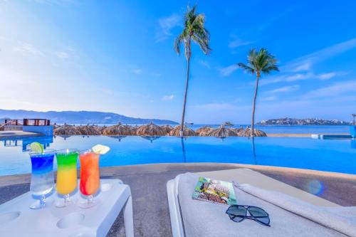 a table with two drinks on it next to a pool at Krystal Beach Acapulco in Acapulco