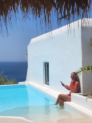 a woman sitting on a bench next to a swimming pool at ELLI TROPiCAL LUXURY SUITES SUNSET-INFINITY POOL- SEA SIDE-NEAR CENTER PARKING in Mikonos