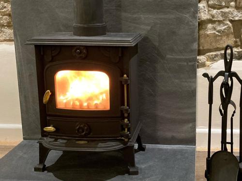 a wood stove with a fire in a room at Bee Cottage in East Lydford