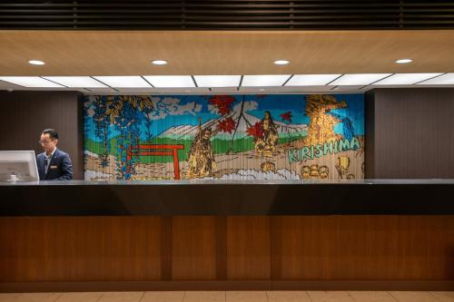 a man standing at a counter with a large mural at Kirishima Kokusai Hotel in Kirishima