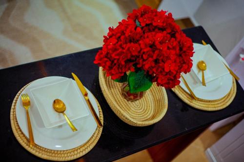 two plates and a vase of red flowers on a table at Splash Mtwara Apartments in Nkunjila