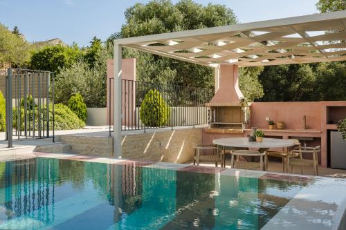 a swimming pool with a table and a pergola next to a house at Majestic Stone Villa Sea View Pool in Andipáta Erísou