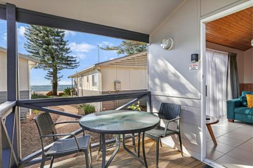 a balcony with a glass table and chairs at Kendalls Beach Holiday Park in Kiama