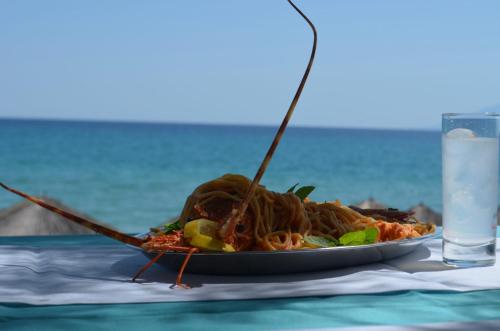 a plate of food with noodles on a table with a glass of water at Grand Beach Hotel Thassos in Limenaria