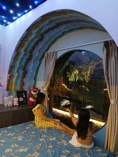 two young girls sitting on a bed looking at a window at paparazzi homestay in Xuyên Mộc