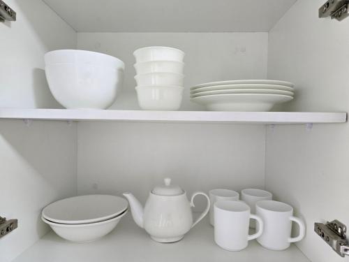 a shelf with white bowls and plates and cups at Cosy Homes in Suva - Home That Hugs You! in Suva