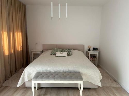 a white bedroom with a white bed with a bench at Apartament NADJEZIORNA EŁK in Ełk