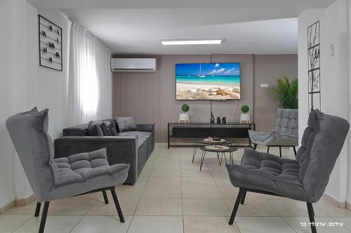 a living room with a couch and chairs and a tv at וילה ויליז'ן in H̱azon