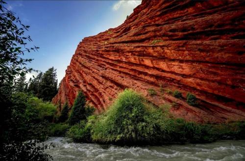 a red rock cliff next to a river next to a mountain at Yurt Camp Town of heavenly mountains " Kyz Zhibek" in Dzhetyoguz