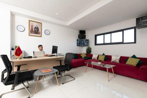 a man sitting at a desk in a living room with a red couch at Garden Bay Signature AppartHotel in Casablanca
