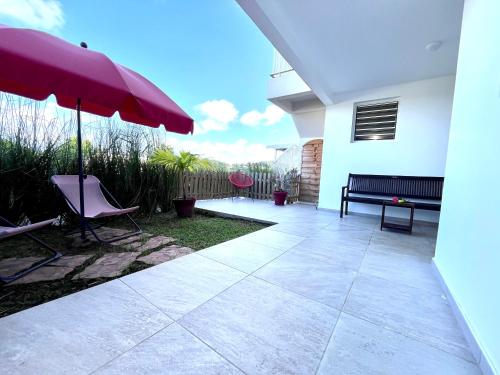 a patio with a bench and an umbrella at Appartement Cosy La Vanille 1 in Ducos
