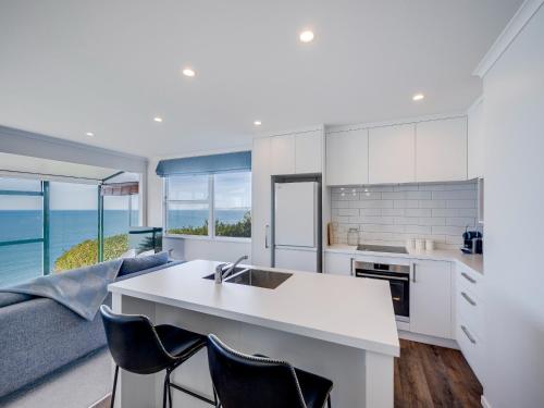 a kitchen with white cabinets and a kitchen island with chairs at Cape View - Napier Holiday Home in Napier