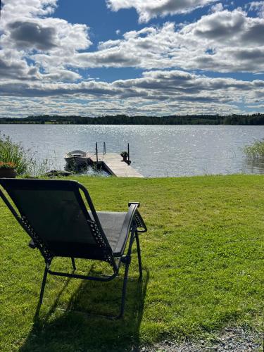 a chair sitting on the grass next to a lake at Sommarstuga med sjötomt och brygga in Hedemora