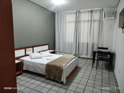 a bedroom with a bed and a table and a window at Hotel Aeroporto Ltda in Vitória