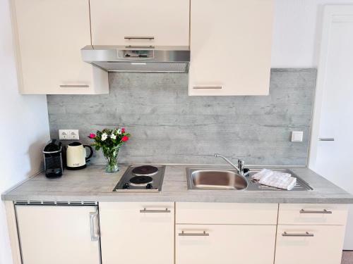 a kitchen with white cabinets and a sink and flowers at Inselsünn Hotel und Apartments in Spiekeroog