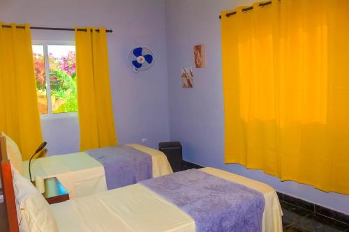 two beds in a room with yellow curtains at Hotel Pousada Venus in São Filipe