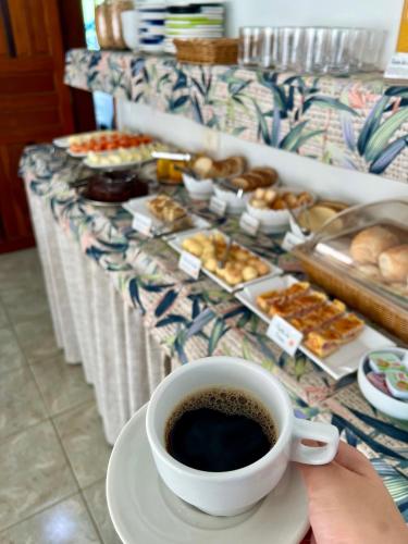 een persoon met een kop koffie en een tafel vol gebak bij Pousada Serrate in Ubatuba