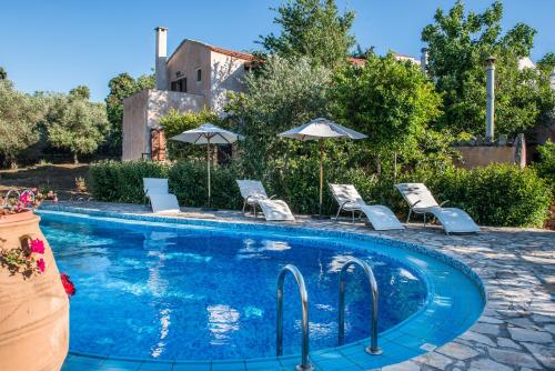 a swimming pool with chairs and umbrellas in a yard at Antheia Houses in Vamos