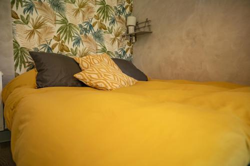 a yellow bed with three pillows on top of it at La Parenthèse Campagnarde in Richarville