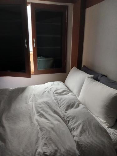 an unmade bed in a room with two windows at 4F, Welcome International traveller, long stay in Busan