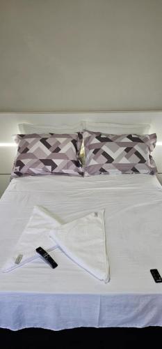 a white bed with two remote controls on it at Lugar Aconchecante 2 Ap 102 in Palhoça