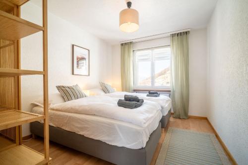 a bedroom with a bed with white sheets and a window at Castor Peak Apartment in Täsch