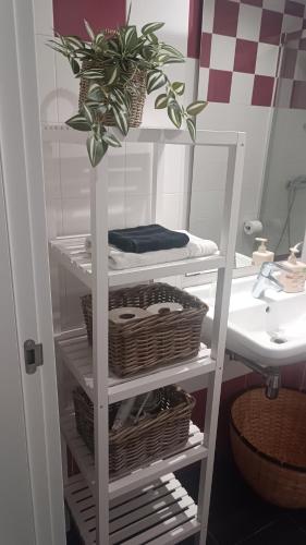 a white shelf with baskets and a plant in a bathroom at Apartamento Galería Cine Colón in Ribadeo