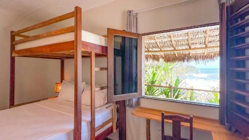 a bedroom with bunk beds and a window with the beach at Che Brazil Pousada in Cruz