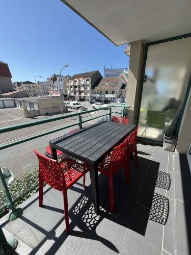 Una mesa negra y dos sillas rojas en un balcón. en Appartement proche mer, en Bray-Dunes