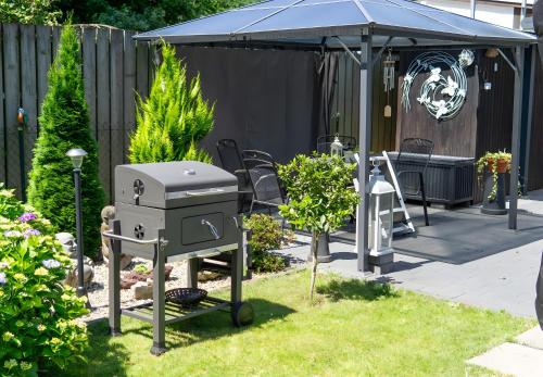 a barbecue grill in a garden with a blue canopy at Ferienhaus Zissi in Wegberg