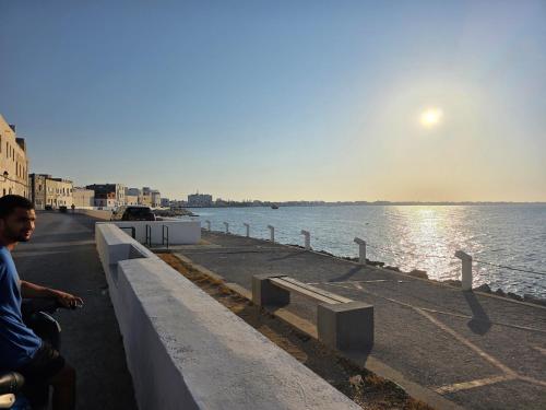 a man sitting on a bench next to the water at Merveilleuse Villa à Borj El Ras in Mahdia