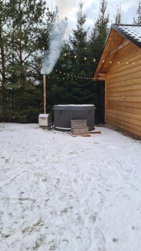 a snow covered yard with a building with smoke at Drewniana chata in Cisówek
