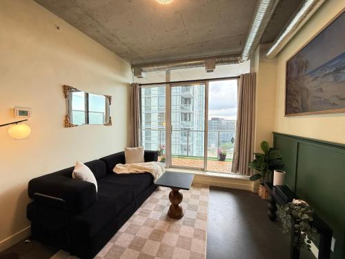 a living room with a black couch and a large window at Stylish Condo, Riverview, Downtown East Village, Mins to Stampede, Saddledome in Calgary