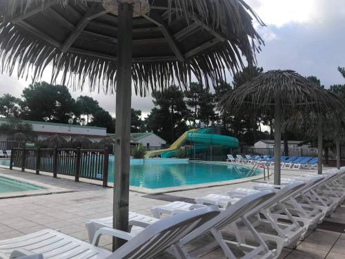 a swimming pool with white chairs and an umbrella and a resort at Camping 4 Étoiles Mobilhome Chez Jéjé et Fredo in Saint-Jean-de-Monts