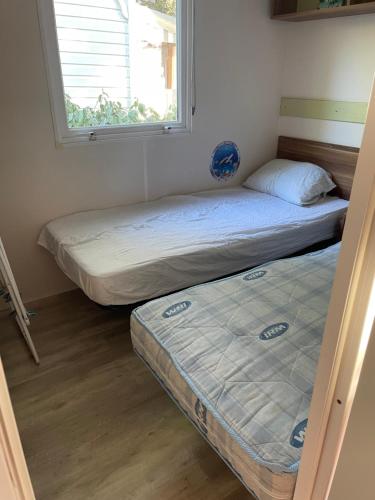 two beds in a room with a window at Camping 4 Étoiles Mobilhome Chez Jéjé et Fredo in Saint-Jean-de-Monts