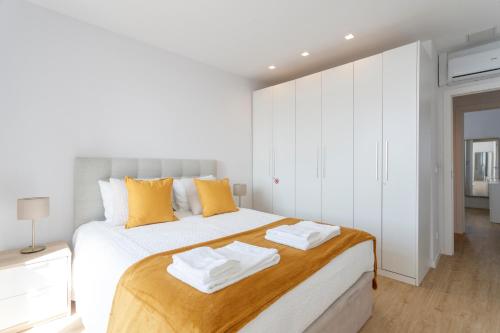 a white bedroom with a large white bed with yellow pillows at Cozy Apartment for Family and Group of Friends in Linda-a-Velha