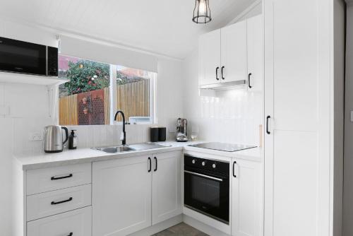eine Küche mit weißen Schränken und einer Spüle und einem Fenster in der Unterkunft Charming 2-Bed House in North Hobart in West Hobart