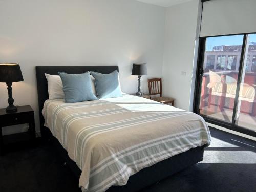a bedroom with a bed with blue pillows and a window at PROMENADE TOWERS 2 Bedroom Apartment with City Views on the Geelong Waterfront - 506 in Geelong