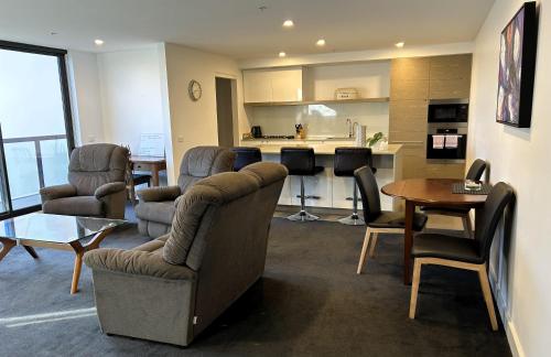 a living room with a couch and chairs and a kitchen at PROMENADE TOWERS 2 Bedroom Apartment with City Views on the Geelong Waterfront - 506 in Geelong