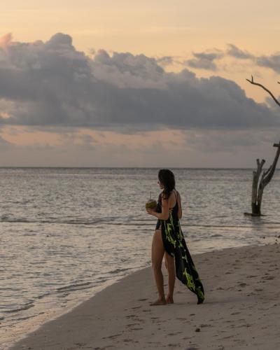 a woman standing on the beach with a drink at Kirulhiya Maldives - Omadhoo in Omadhoo