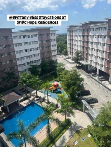 a resort with a pool and palm trees and buildings at Brittany Bliss Staycations at SMDC HOPE RESIDENCES in Trece Martires