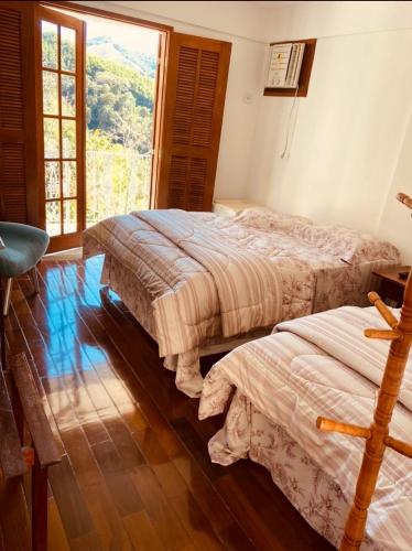two beds in a room with a large window at Pousada Pedacinho do Céu in Conservatória