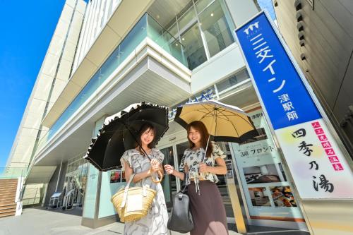 two women standing in front of a building holding umbrellas at Sanco Inn Tsu Ekimae in Tsu
