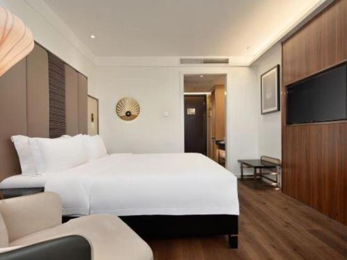 a bedroom with a large white bed and a tv at Jinjiang Metropolo Haikou East High Speed Railway Station Normal University in Haikou