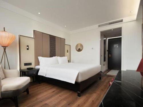a bedroom with a large white bed and a chair at Jinjiang Metropolo Haikou East High Speed Railway Station Normal University in Haikou