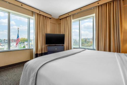 a bedroom with a bed and a tv and windows at Cambria Hotel Akron - Canton Airport in Uniontown