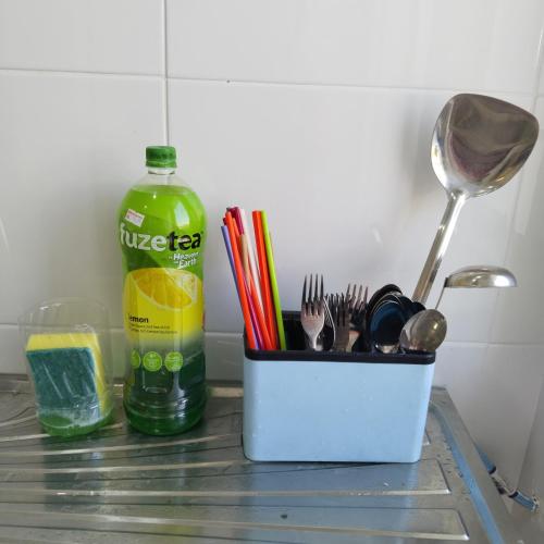 a container of utensils on a counter with a bottle of soda at Happpy Impiana Guest House in Bentong