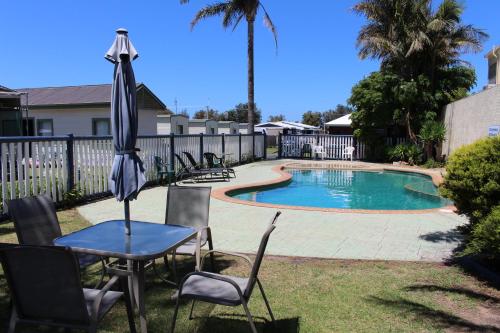 a table and chairs with an umbrella next to a pool at Golden Terrace Holiday Park in Lakes Entrance