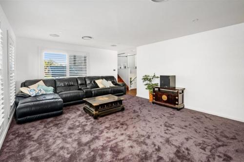 a living room with a black leather couch and a table at Peace In Paradise near Nelson Bay- waterviews, spa, adventures in Lemon Tree Passage